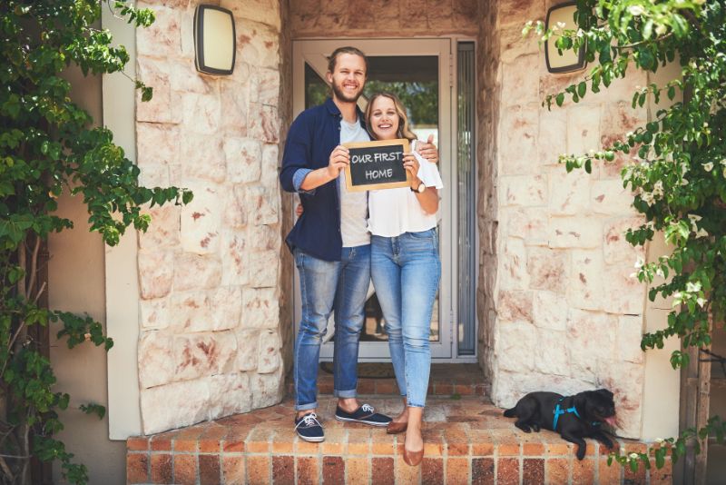 a couple holding a board saying "our first home"